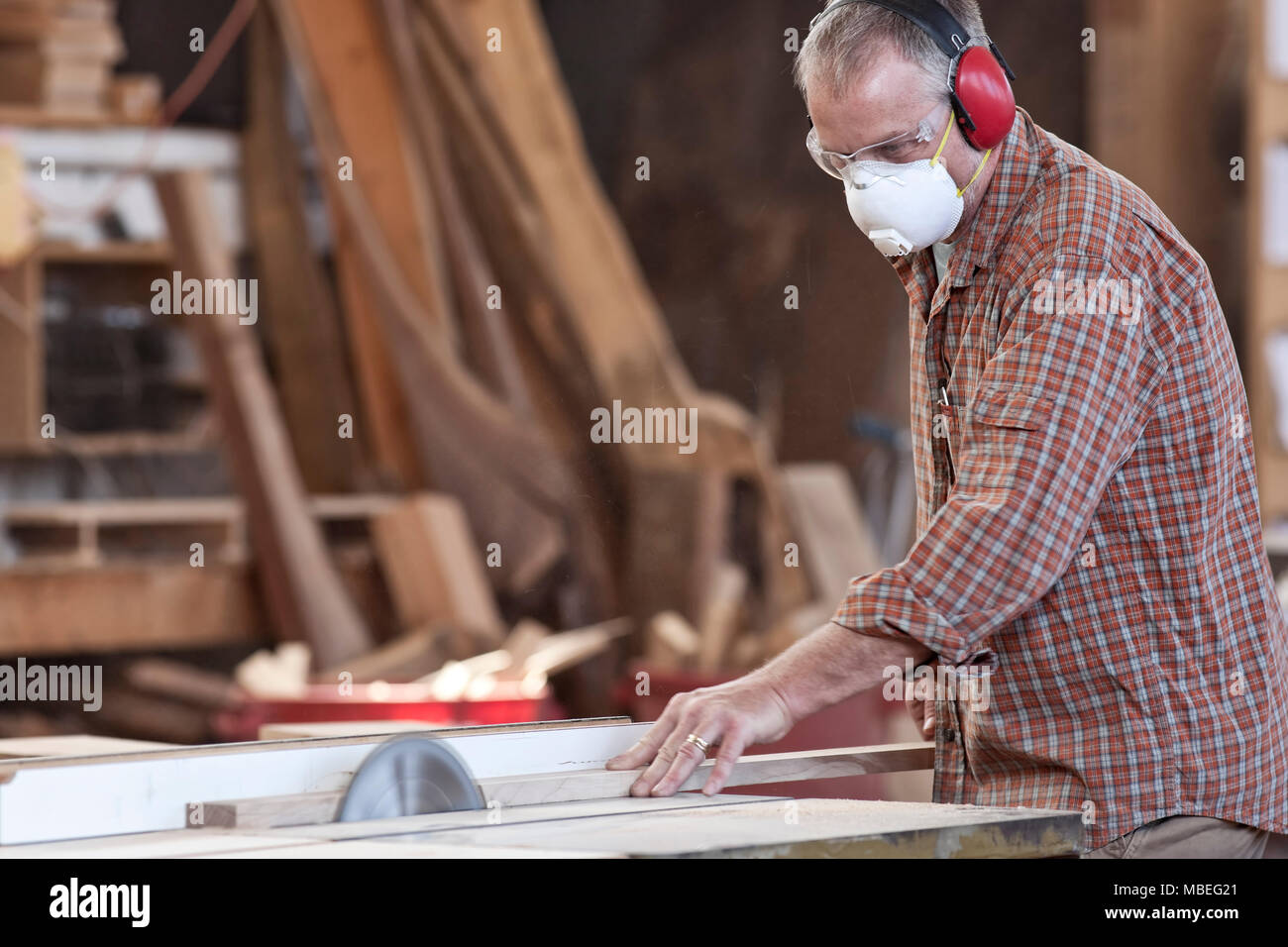 Caucasian man factory worker wearing une protection auditive et un nez masque antipoussière, tandis que la coupe de bois sur une scie de table. Banque D'Images