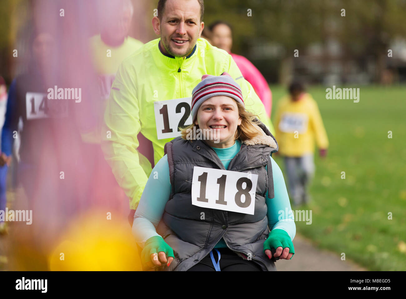 Portrait man poussant smiling woman in wheelchair at charity race in park Banque D'Images