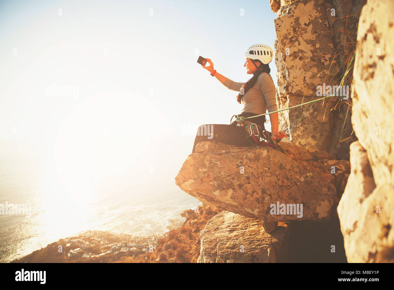 Female rock climber avec téléphone appareil photo photographier sunny vue sur l'océan Banque D'Images