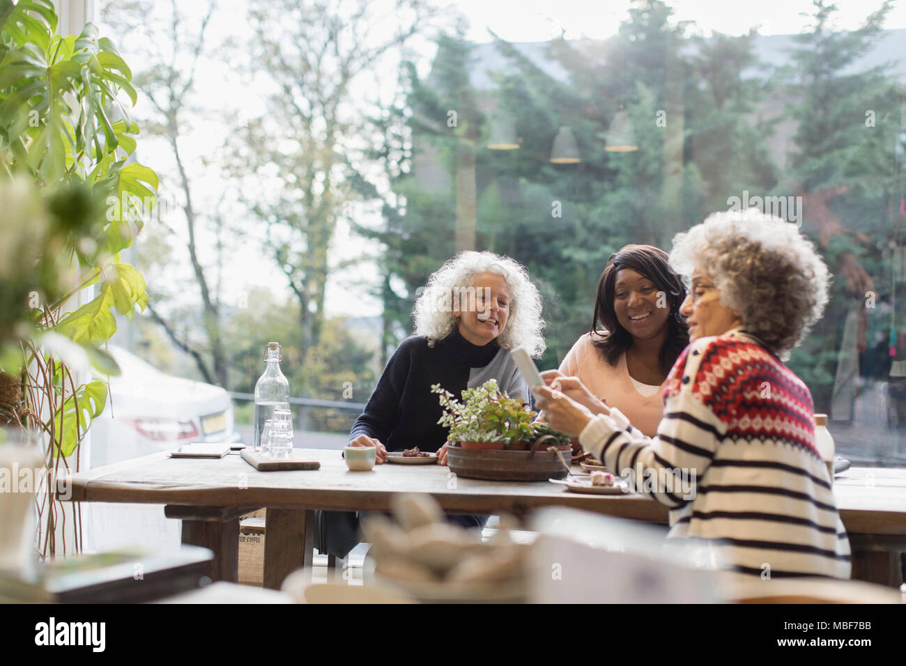 Smiling women amis à l'aide de smart phone at cafe table Banque D'Images