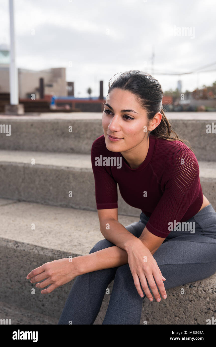 Jeune sportive brunette sitting on stairs portant des vêtements fitness avec cheveux attachés en arrière Banque D'Images