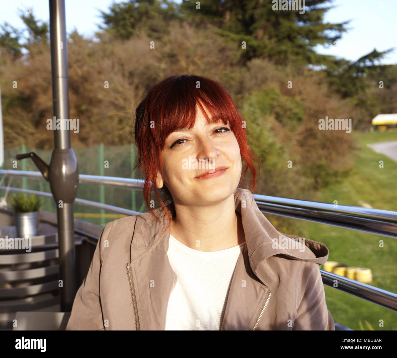 Belle jeune femme rousse assise sur la terrasse du café sur la journée de printemps ensoleillée et looking at camera and smiling Banque D'Images
