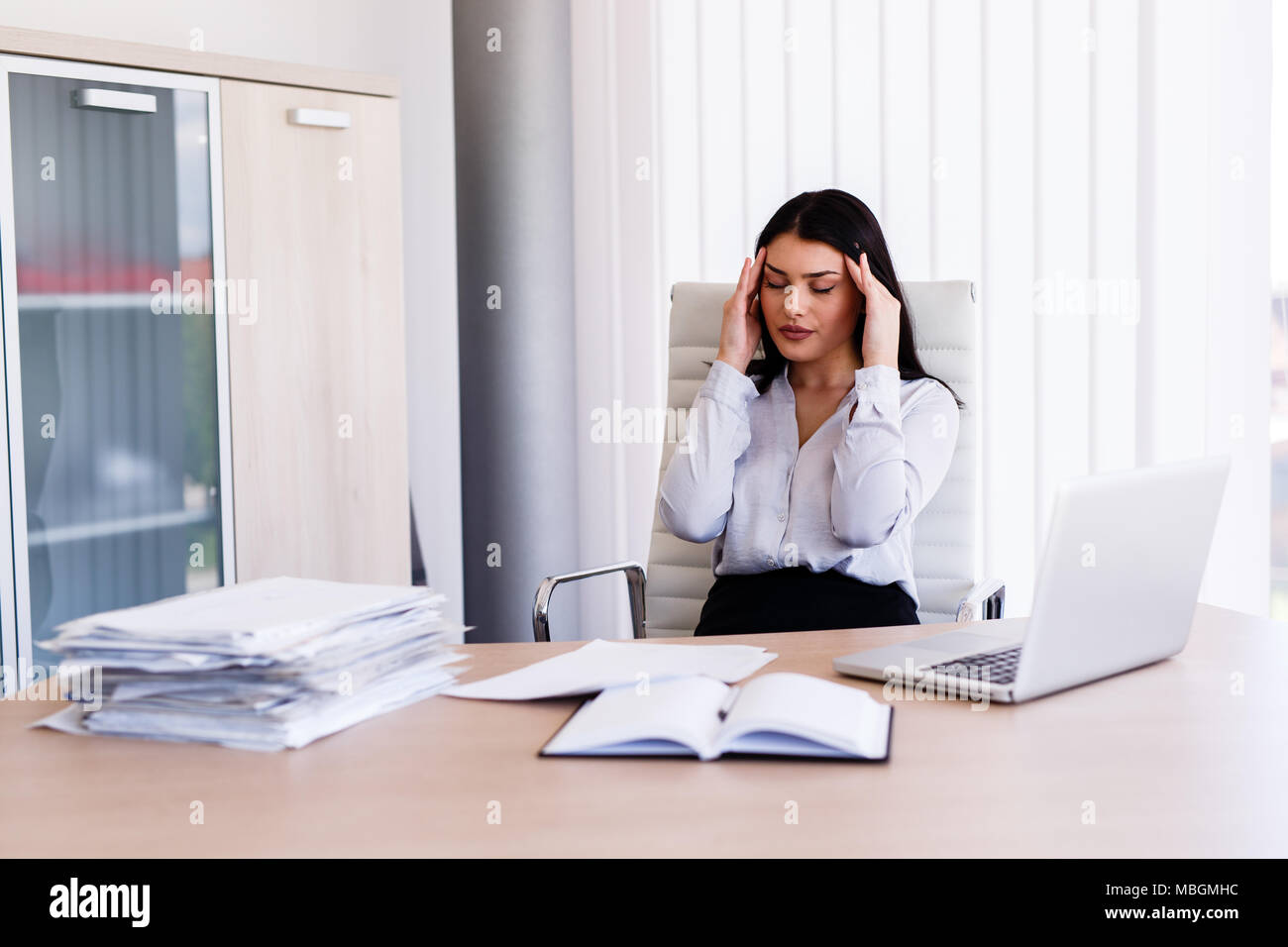 Businesswoman having maux de tête dans son bureau après avoir fait un travail très dur Banque D'Images