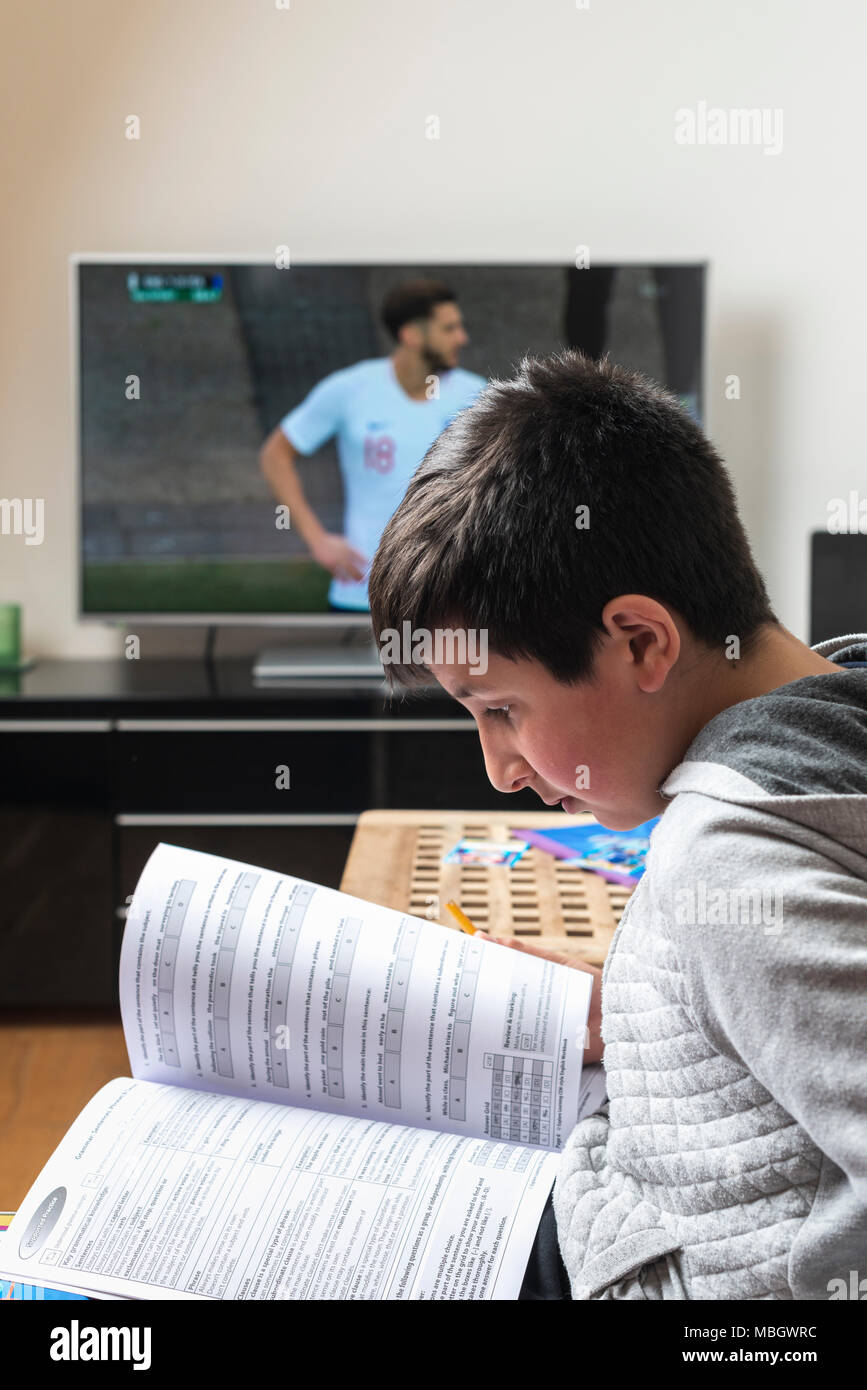 UK-écolier, 10 ans ,essayer d'étudier tout en match de football joue à la télévision Banque D'Images