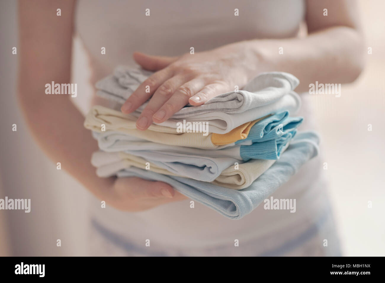 Tri des vêtements de bébé nouveau-né de la mère pour le repassage à domicile dans le cadre des activités quotidiennes dans les services de garde, selective focus Banque D'Images