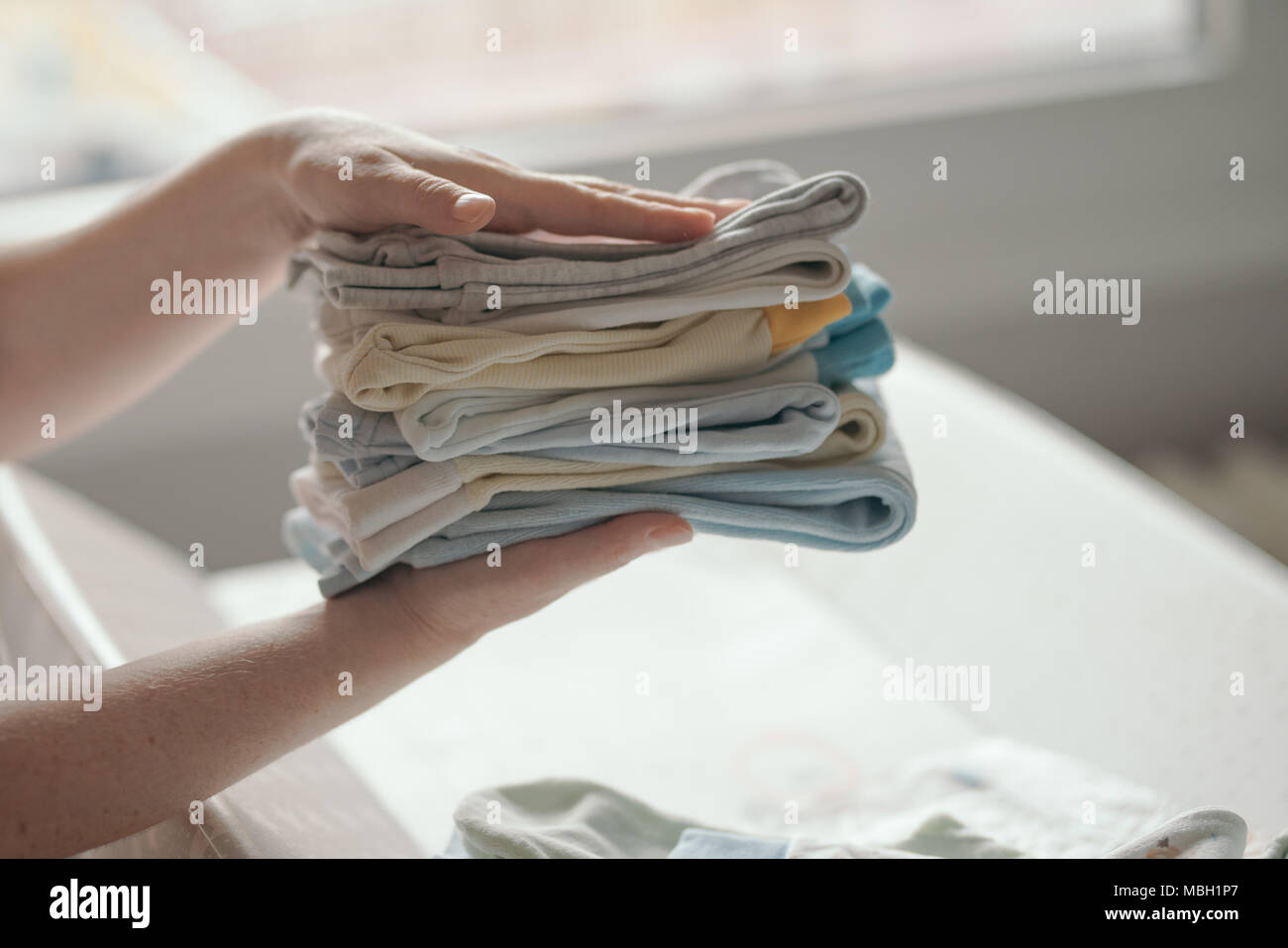 Tri des vêtements de bébé nouveau-né de la mère pour le repassage à domicile dans le cadre des activités quotidiennes dans les services de garde, selective focus Banque D'Images