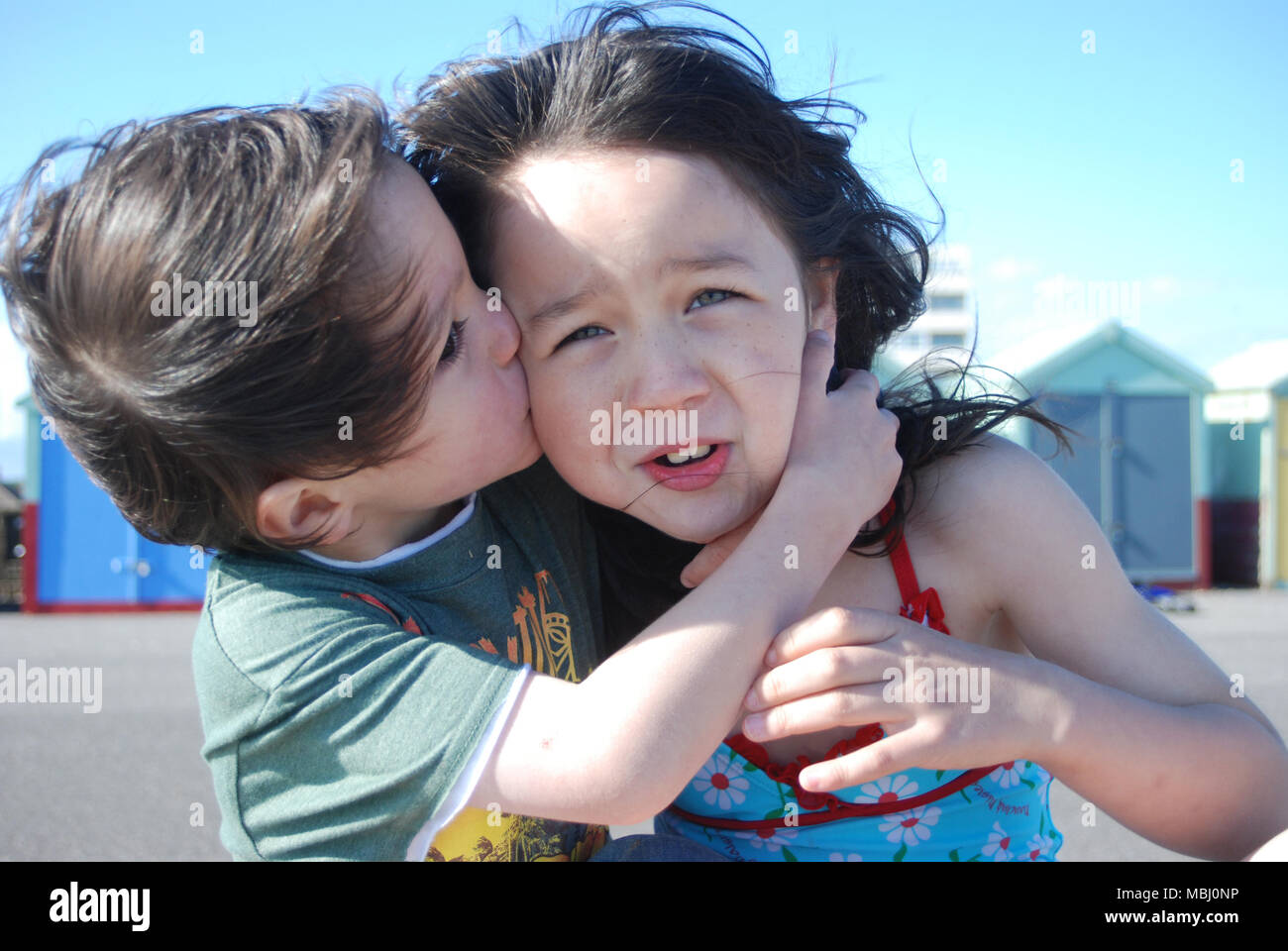 Les enfants âgés de 5 et 7 Frère 5 hugging sa sœur en face de cabanes de plage Banque D'Images