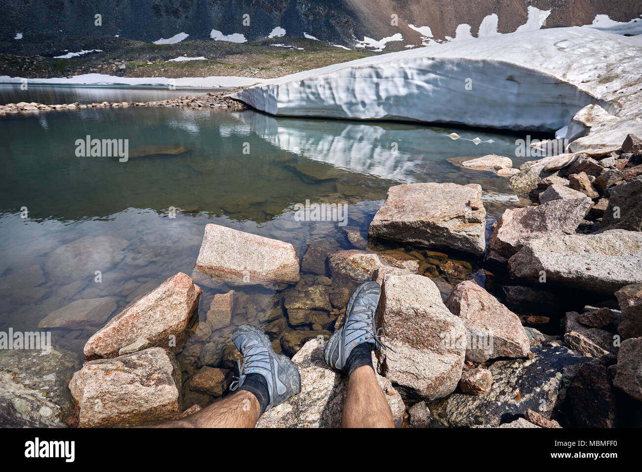 Les jambes de l'homme dans le suivi des chaussures et de la vue sur le lac glacier enneigé dans les montagnes Banque D'Images