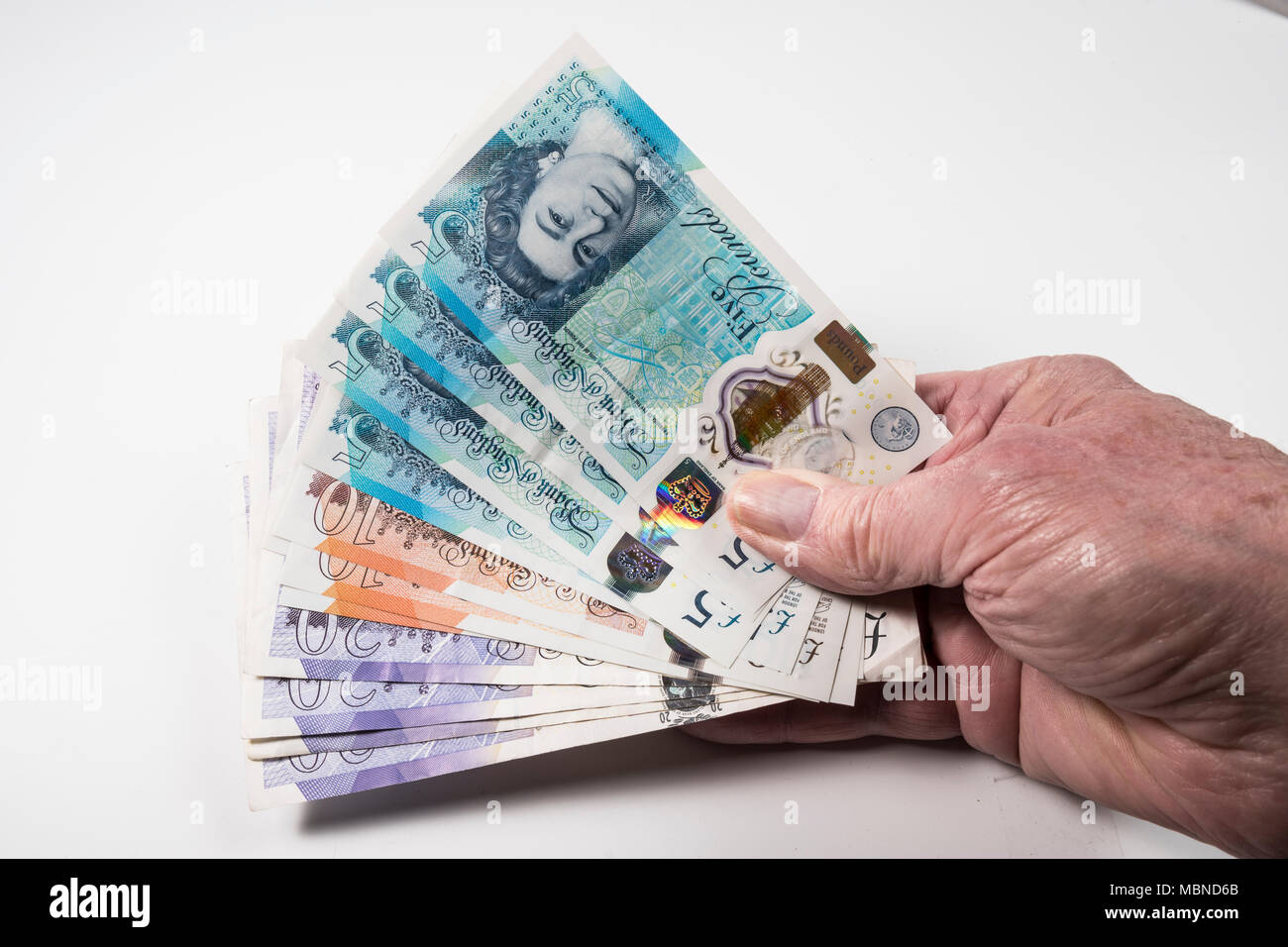 Un mâle hand holding UK argent, £5 pound, £10 et £20 pound pound notes dans un ventilateur Banque D'Images