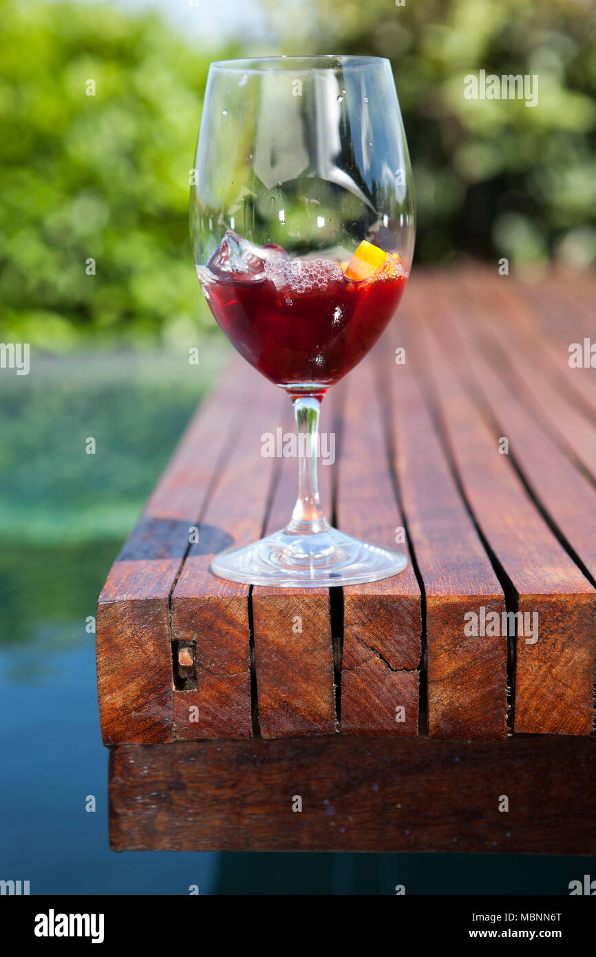 Shot vertical d'un verre de vermouth rouge avec des cubes de glace à proximité d'une piscine à la campagne Banque D'Images