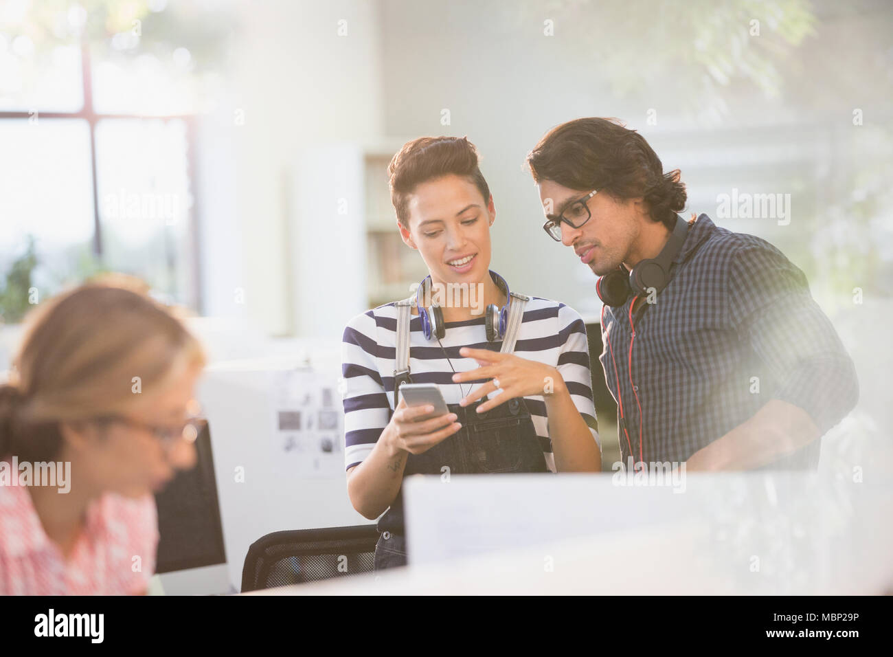 Les gens d'affaires créatifs avec des écouteurs à l'aide de smart phone in office Banque D'Images