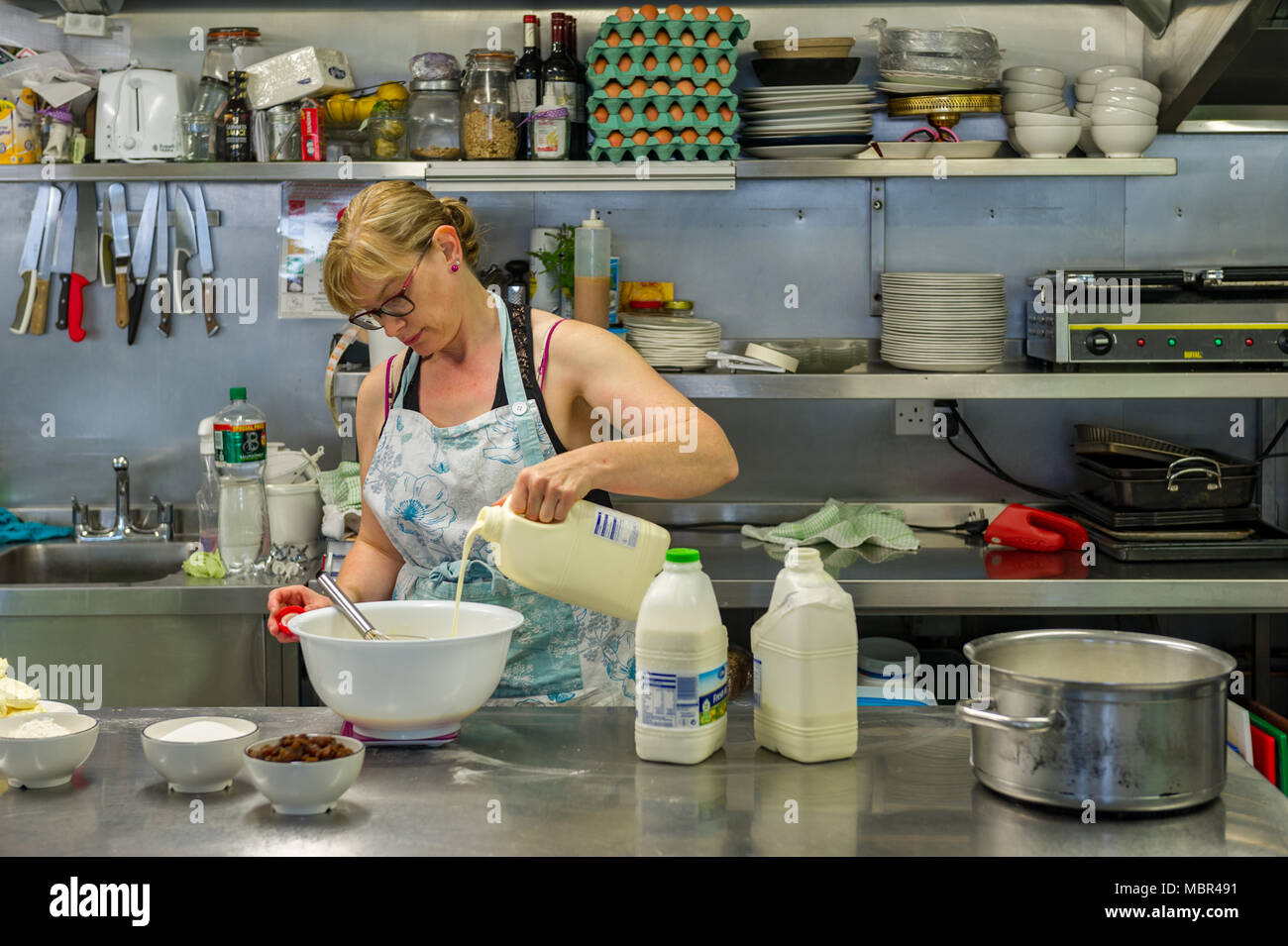 Femme verse du lait dans un bol alors que la cuisson dans une cuisine commerciale dans un café en Irlande. Banque D'Images
