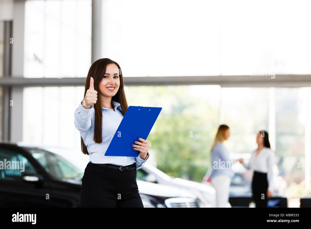 Business Woman standing et showing Thumbs up alors qu'il y a son collègue en arrière-plan faire handshake Banque D'Images