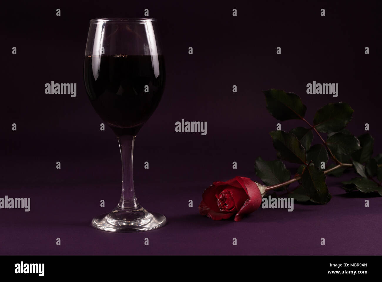 Verre à vin rouge et rose fleur sur fond violet foncé, clé faible Banque D'Images