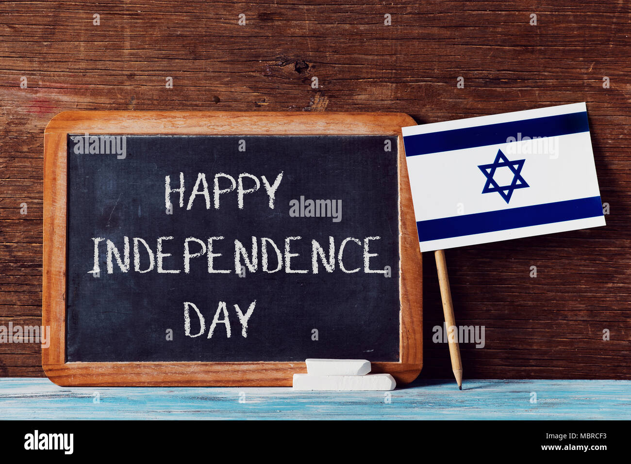Un tableau en bois avec la joyeuse fête de l'indépendance du texte écrit en C, quelques morceaux de craie et un drapeau israélien sur une surface en bois rustique Banque D'Images