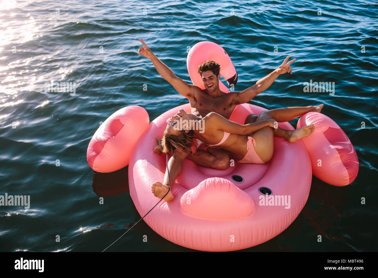 Excitée jeune couple assis sur un jouet gonflable ride derrière un bateau dans la mer et d'avoir du plaisir. L'homme et la femme à cheval sur un jouet gonflable lié à un bateau Banque D'Images
