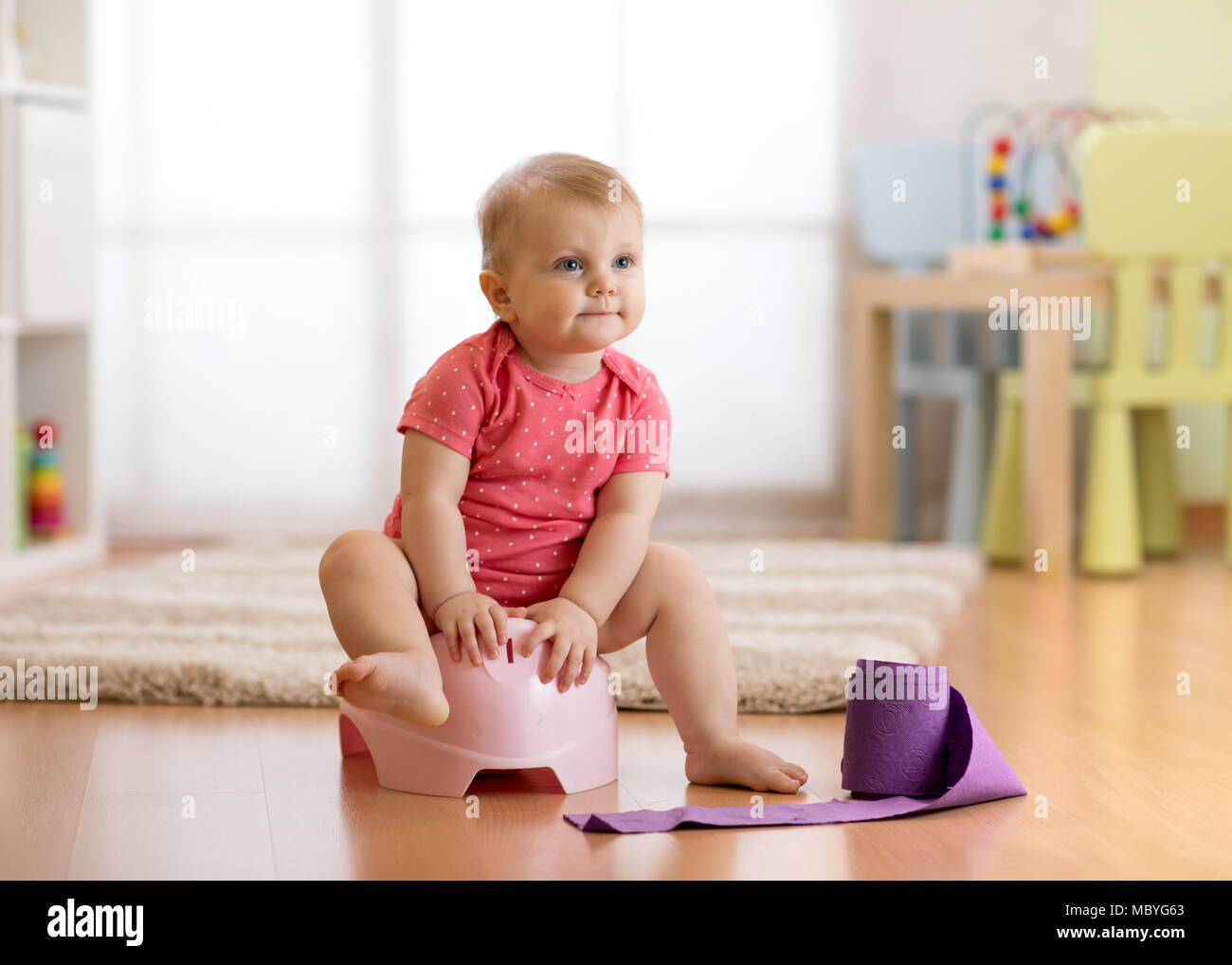 Cute baby sitting sur pot de chambre avec rouleau de papier toilettes Banque D'Images