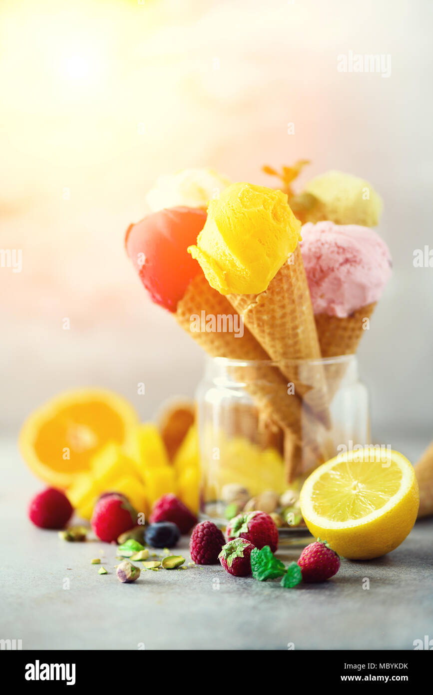 Boules de crème glacée coloré en cônes alvéolés avec différentes saveurs - mangue, citron vert, menthe, pistache, orange, fraises, framboises, bleuets. Concept d'été Banque D'Images