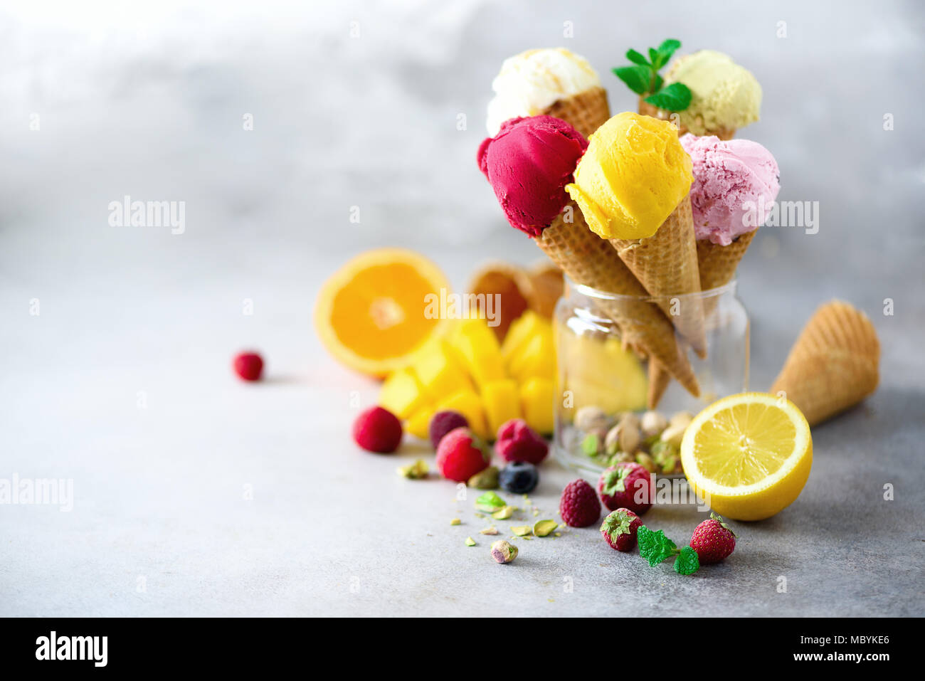 Boules de crème glacée coloré en cônes alvéolés avec différentes saveurs - mangue, citron vert, menthe, pistache, orange, fraises, framboises, bleuets. Concept d'été Banque D'Images