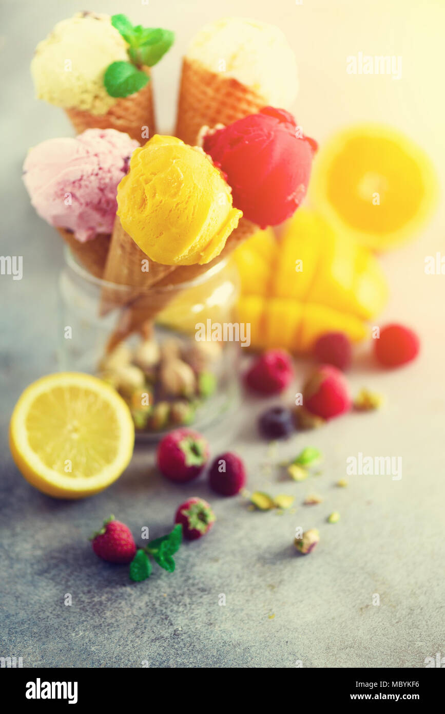 Boules de crème glacée coloré en cônes alvéolés avec différentes saveurs - mangue, citron vert, menthe, pistache, orange, fraises, framboises, bleuets. Concept d'été Banque D'Images