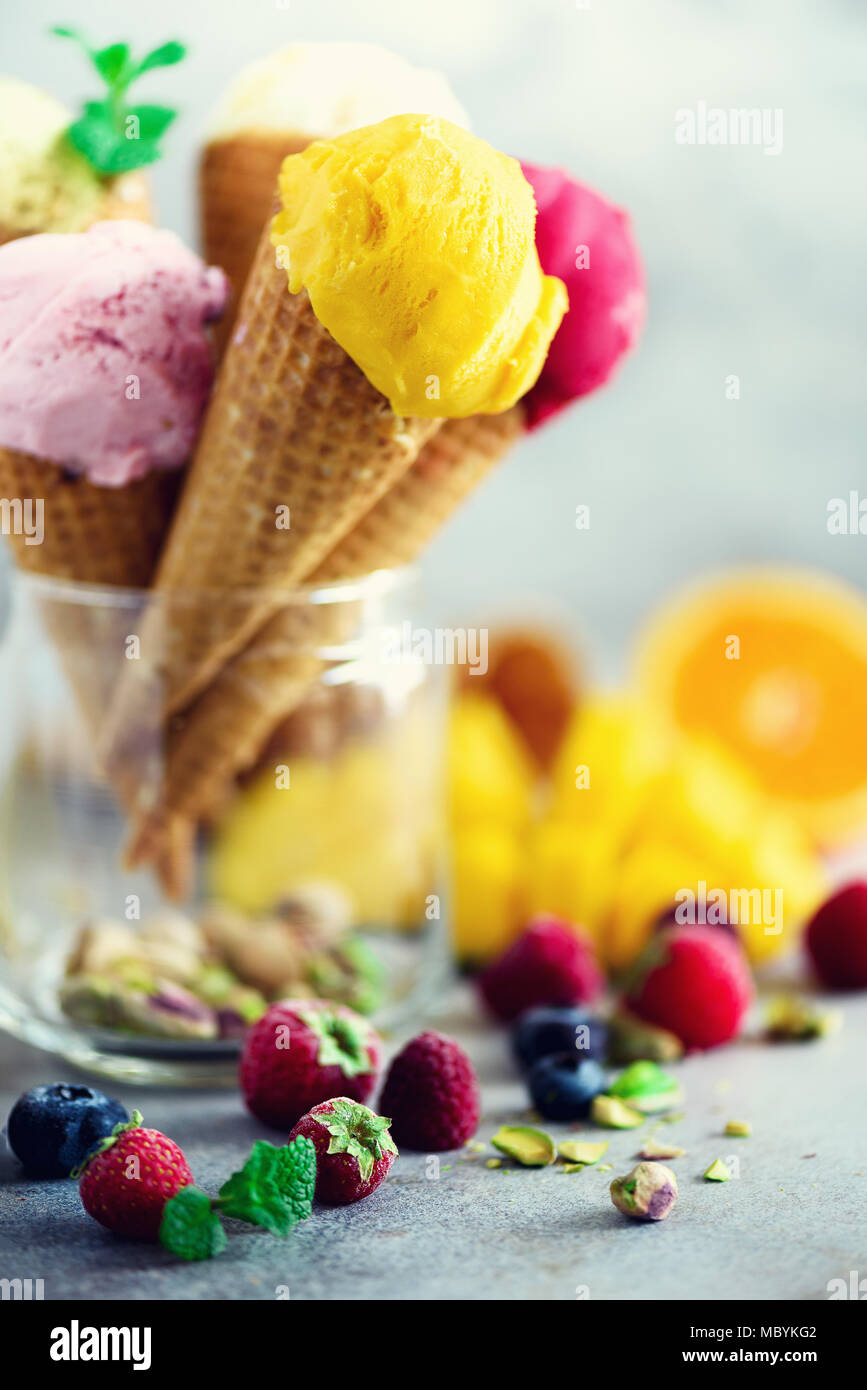 Boules de crème glacée coloré en cônes alvéolés avec différentes saveurs - mangue, citron vert, menthe, pistache, orange, fraises, framboises, bleuets. Concept d'été Banque D'Images