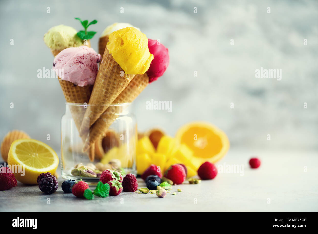 Boules de crème glacée coloré en cônes alvéolés avec différentes saveurs - mangue, citron vert, menthe, pistache, orange, fraises, framboises, bleuets. Concept d'été Banque D'Images