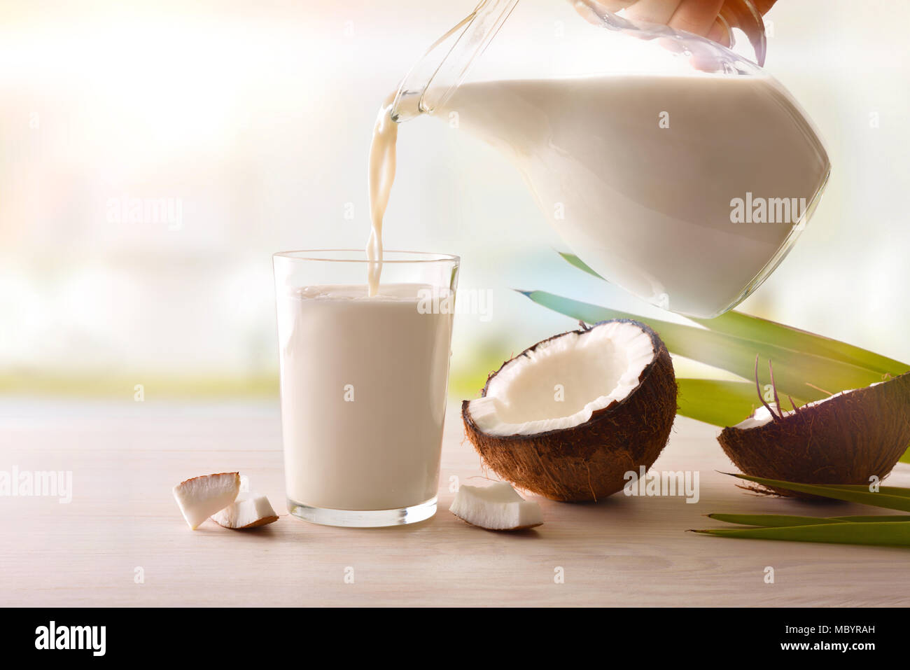 Remplir un verre d'un pot sur une table en bois blanc sur un arrière-plan de cuisine. Autre concept de lait. Vue de face. Composition horizontale. Banque D'Images