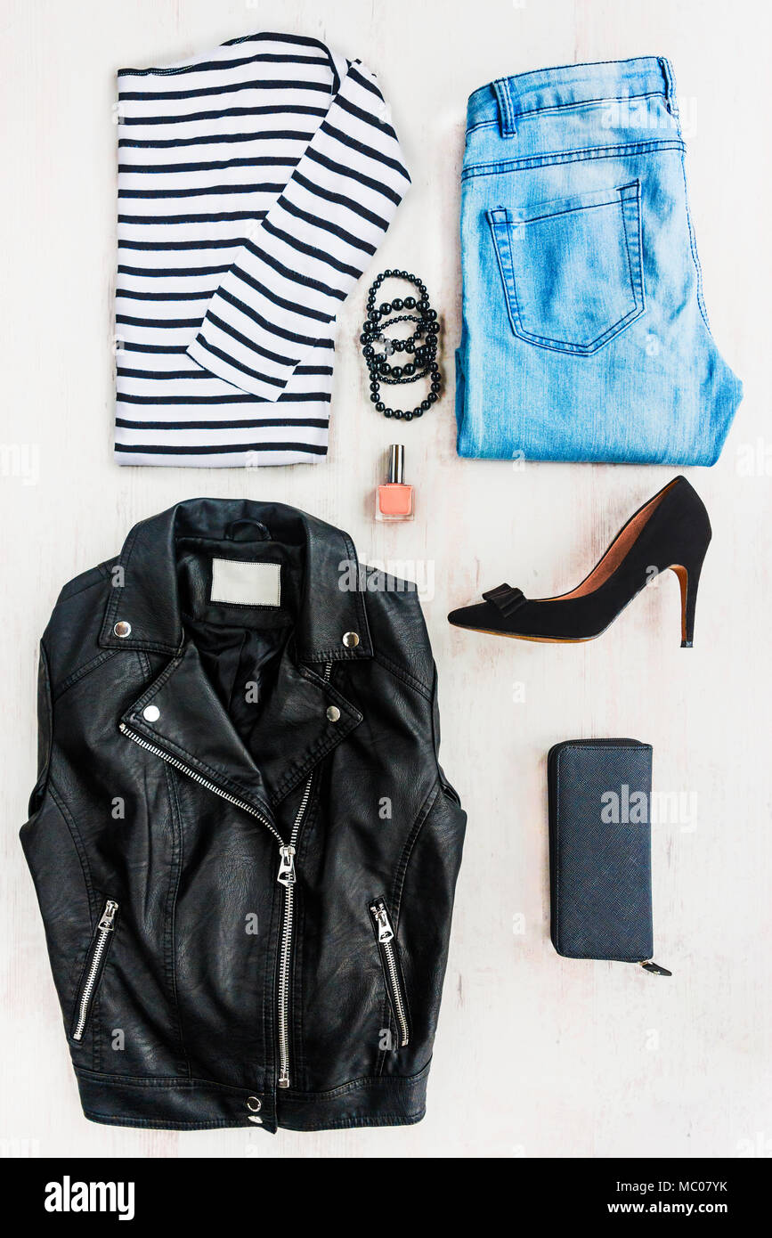 Collage de l'habillement femelle ensemble. Blue Jeans, Chemisier rayé, veste en cuir noir, talons hauts chaussures et accessoires sur fond de bois blanc. Banque D'Images
