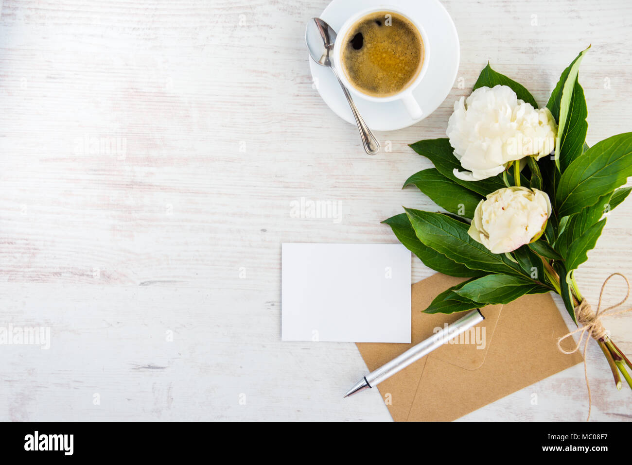 Vue de dessus d'une carte de vœux, vide enveloppe kraft, de pivoines bouquet et une tasse de café plus rustique en bois blanc, arrière-plan. Banque D'Images