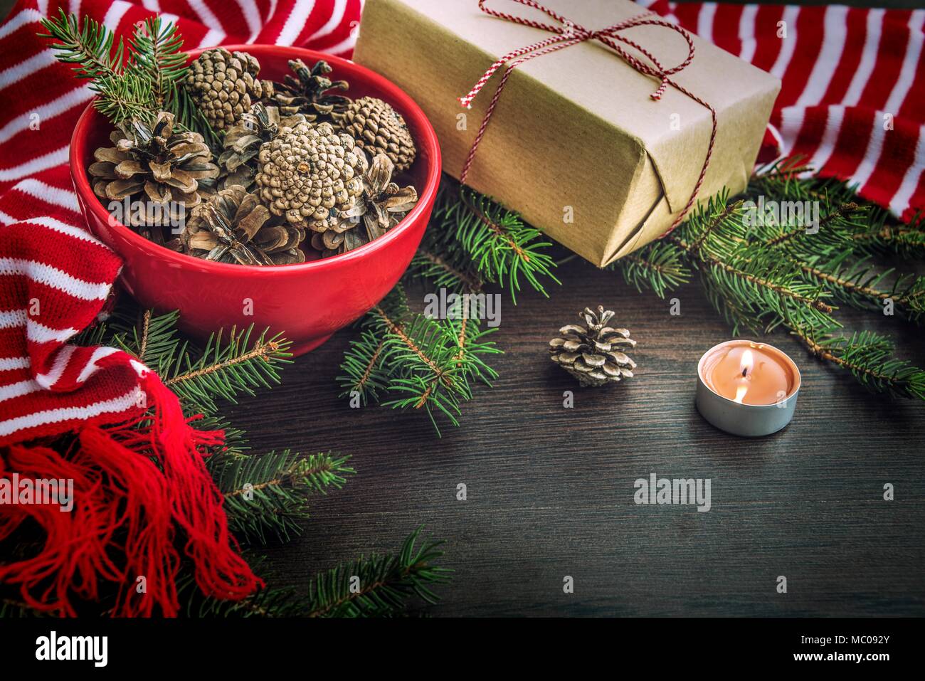 Décoration de Noël - rouge bol plein de cônes de sapin, boîte-cadeau enveloppé dans du papier kraft, des branches de pins, bougie et rouge et blanc à rayures écharpe d'hiver. Chri Banque D'Images