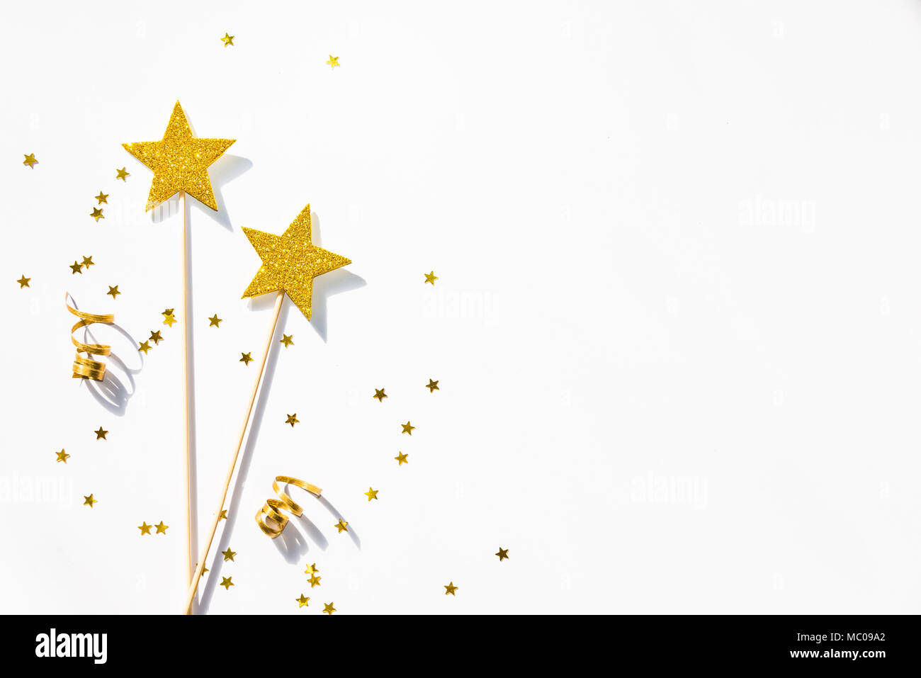 Parti d'or deux baguettes magiques, des sequins et rubans sur fond blanc. Copier l'espace. Banque D'Images