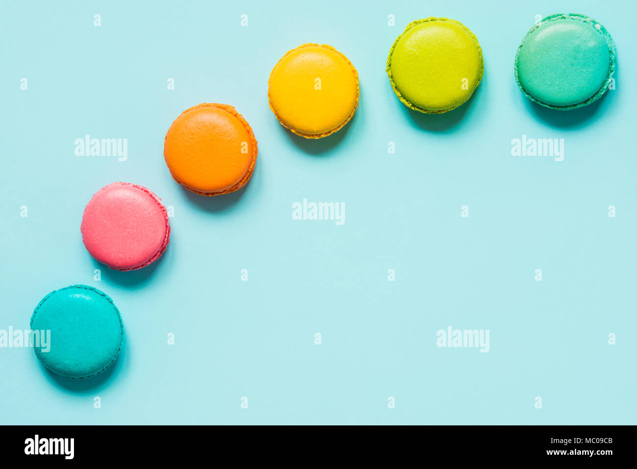Macarons colorés disposés comme arc-en-ciel sur fond bleu. Banque D'Images