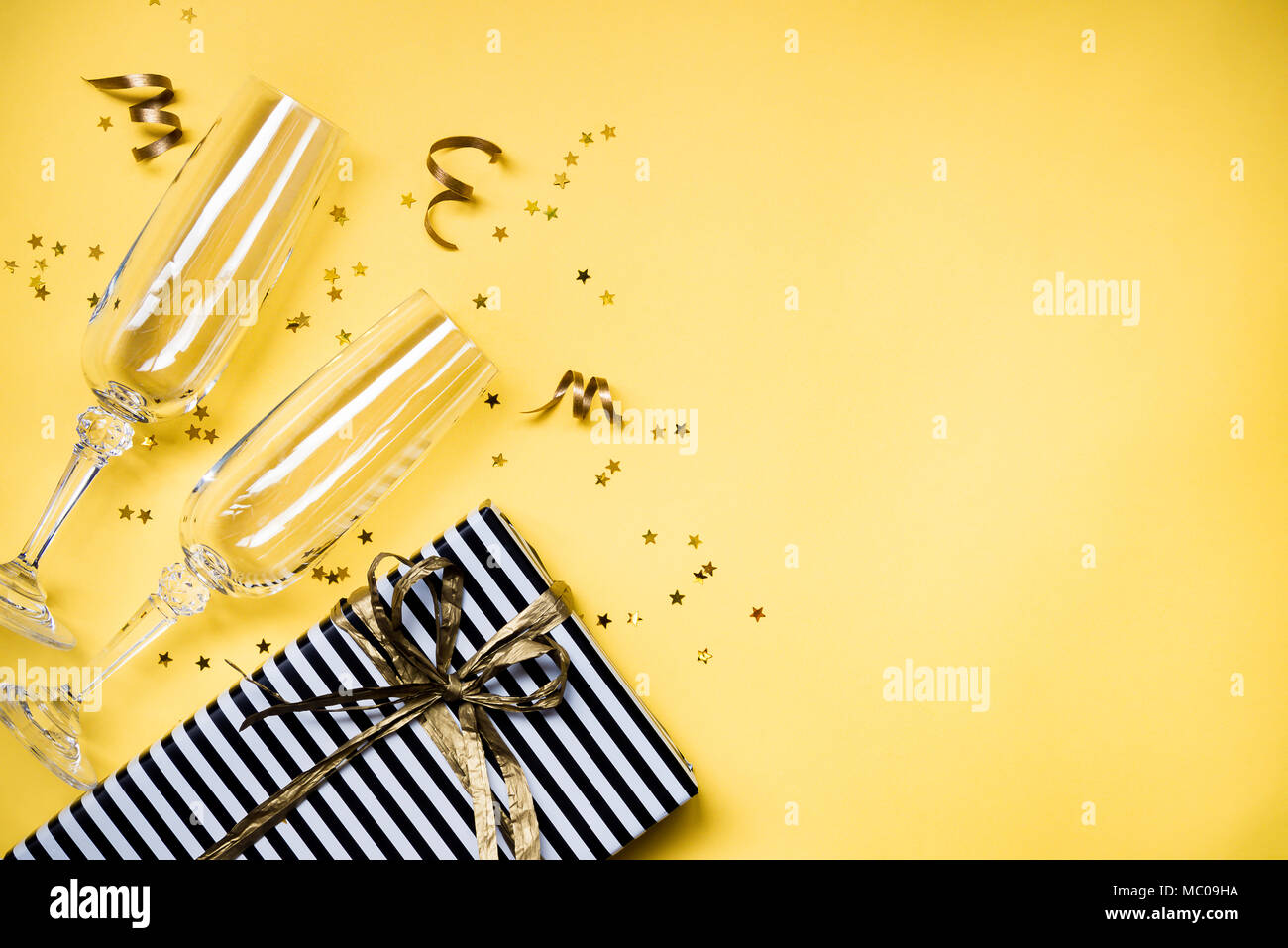 Célébration Contexte - Vue de dessus deux chrystal verres de champagne, une boîte cadeau enveloppé dans du papier rayé noir et blanc, des rubans et des étoiles d'or en forme de Banque D'Images