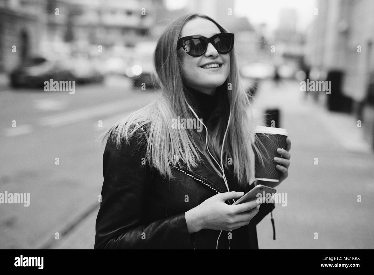 Jolie fille se tenir sur la rue écouter la musique de ses écouteurs et boire le café, un coup de vent Banque D'Images