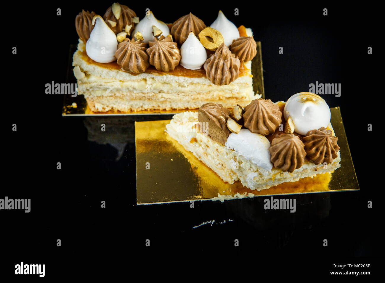 Pièces découpées double couche de gâteau décoré abondamment de Kiev avec crème au chocolat et noix gros plan sur fond noir avec reflet miroir Banque D'Images