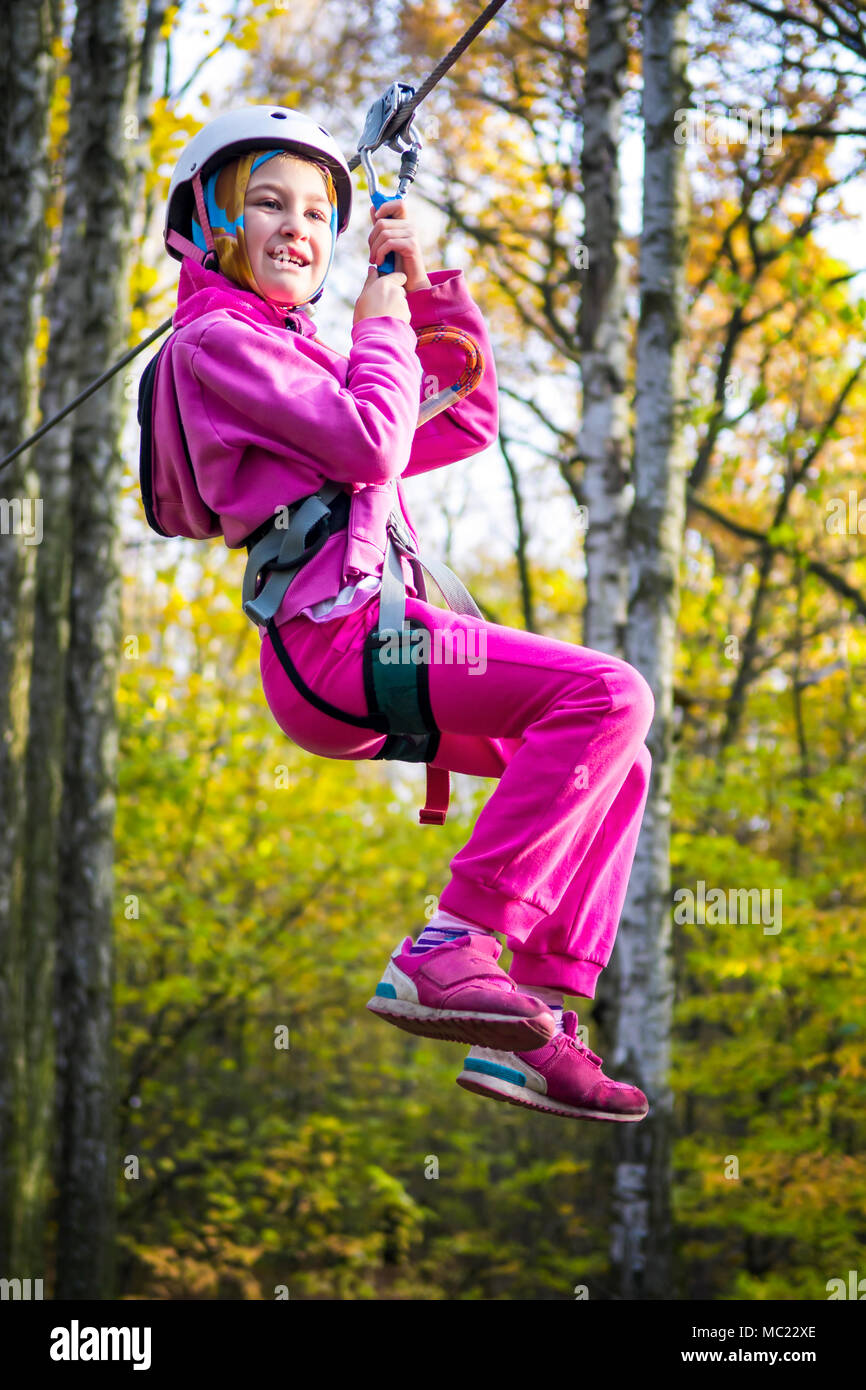 Jeune fille sur la tyrolienne entre les arbres dans un parc d'aventure. Banque D'Images