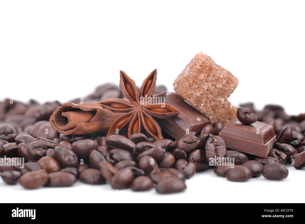 Étoile d'anis, chocolat et sucre en tas de grains de café sur fond blanc Banque D'Images