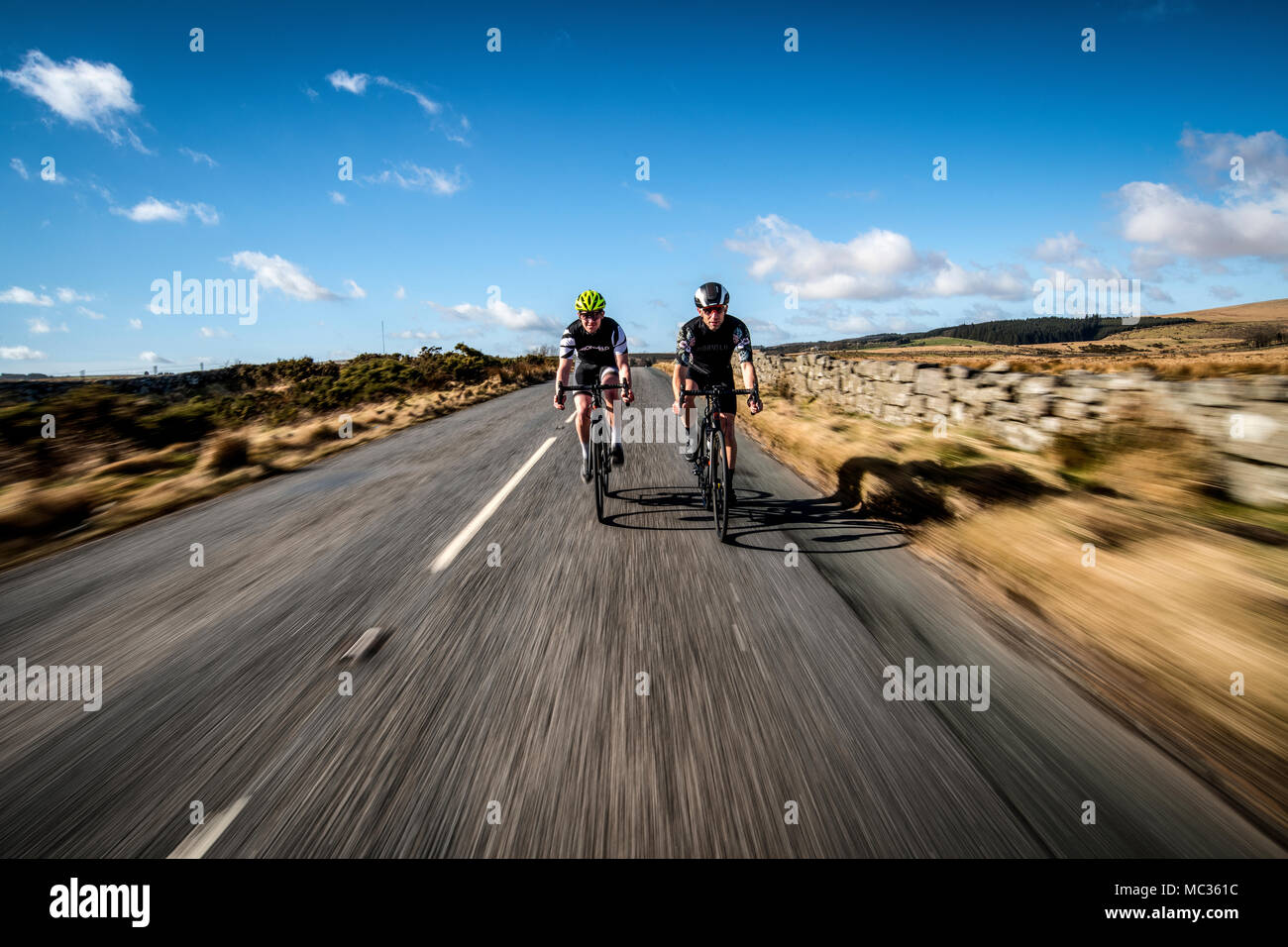 Deux cyclistes roulent le long d'une route à Dartmoor, dans le Devon, Angleterre, Royaume-Uni. Flou de vitesse. Banque D'Images