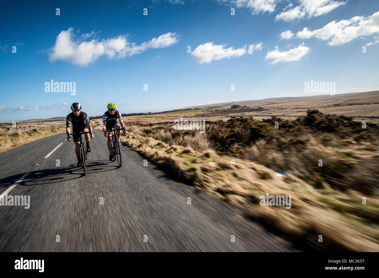 Deux cyclistes roulent le long d'une route à Dartmoor, dans le Devon, Angleterre, Royaume-Uni. Flou de vitesse. Banque D'Images