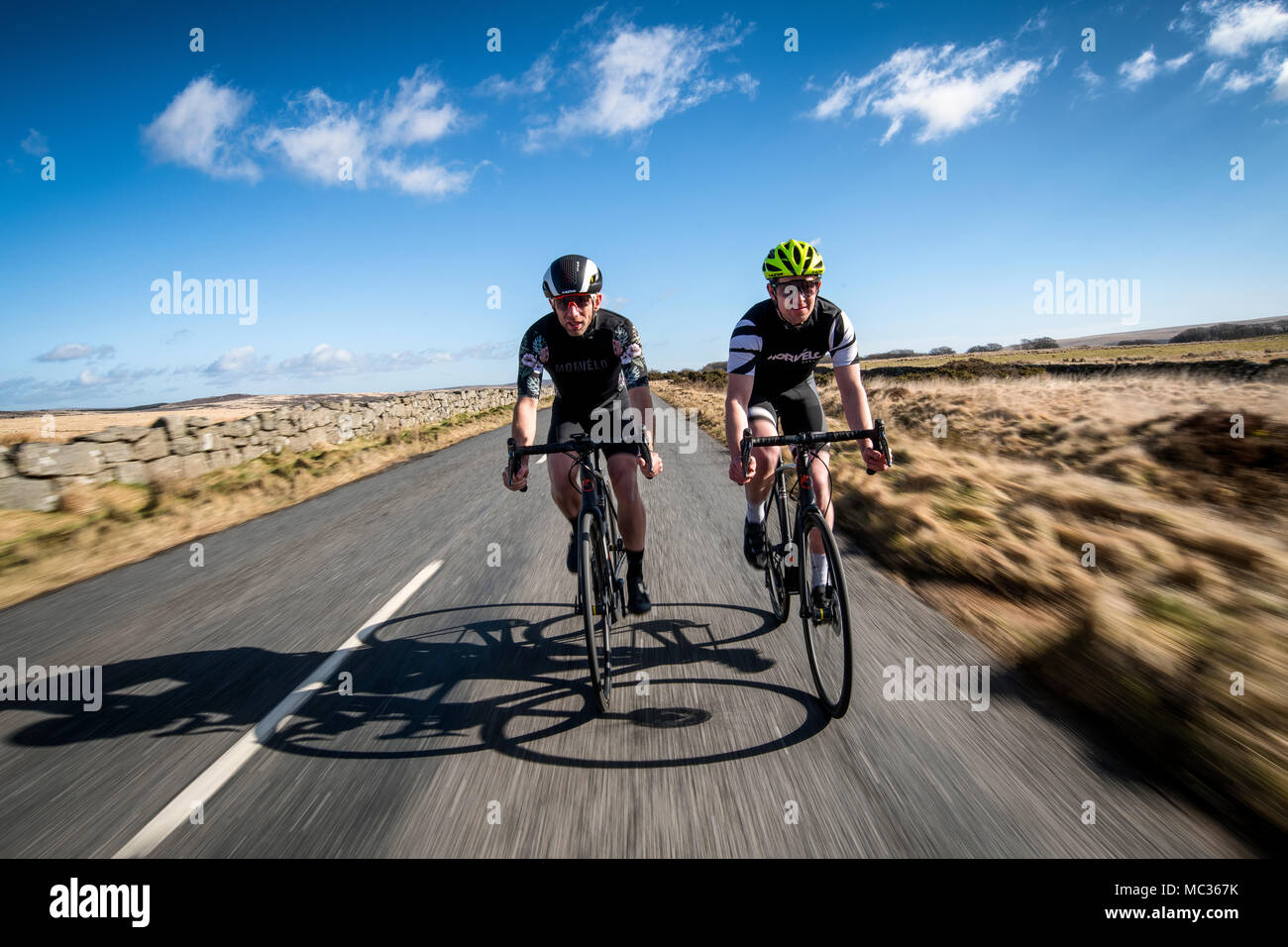 Deux cyclistes roulent le long d'une route à Dartmoor, dans le Devon, Angleterre, Royaume-Uni. Flou de vitesse. Banque D'Images