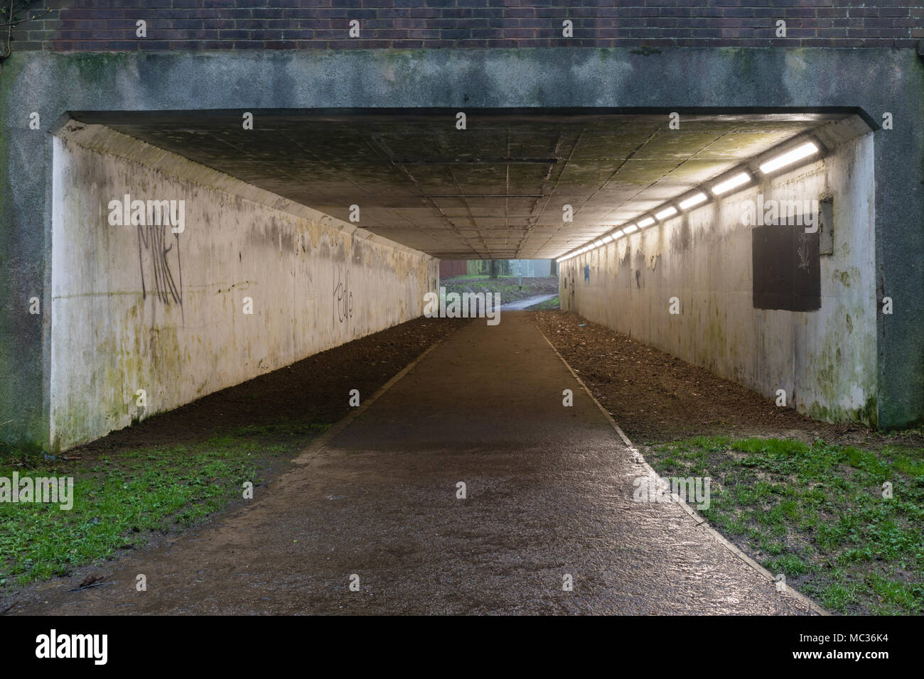 Passage souterrain de béton sous l'Est de façon, Daventry. Le chemin est humide de pluie récente et reflète les lumières dans le passage souterrain. Banque D'Images