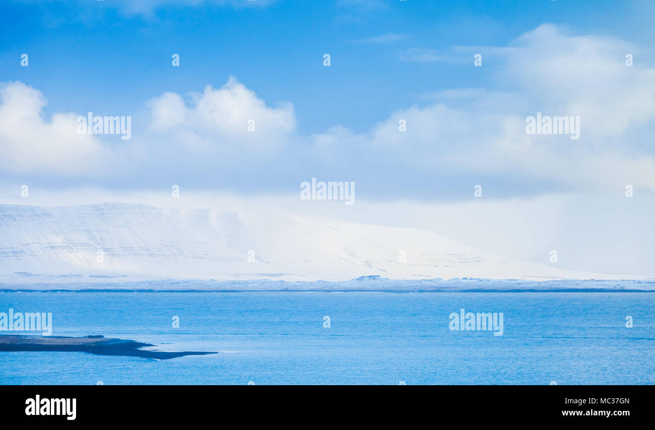Paysage côtier de l'Islande, petite île et montagnes enneigées sur horizon sous ciel bleu. Reykjavik, Islande Banque D'Images
