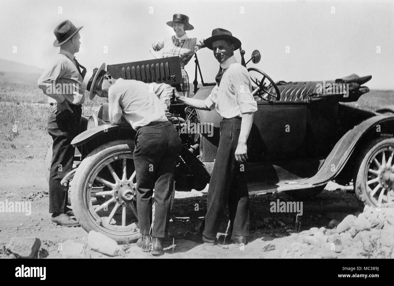 Trois hommes et une femme s'arrêter pour les réparations de voiture sur une route poussiéreuse dans l'Ouest américain, ca. 1925. Banque D'Images