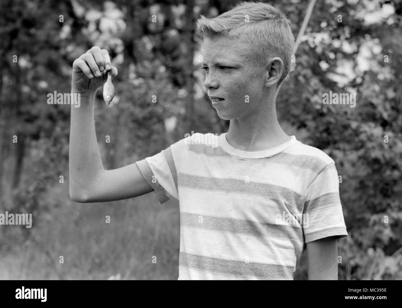 Un jeune garçon semble s'inquiéter au sujet de la taille de ses prises, ca. 1960. Banque D'Images