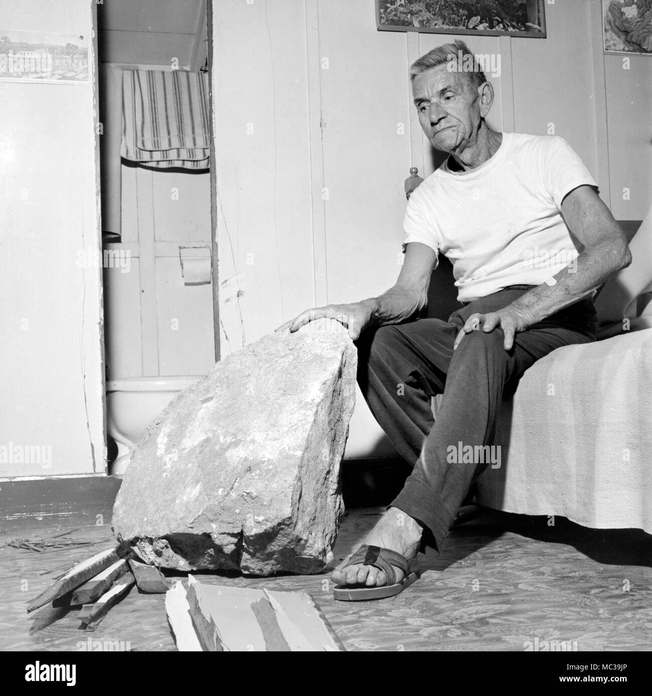 Un homme est assis avec la roche qui est venu s'écraser dans sa maison juste à côté de lui dans son lit après un land slide en Californie, ca. 1961. Banque D'Images