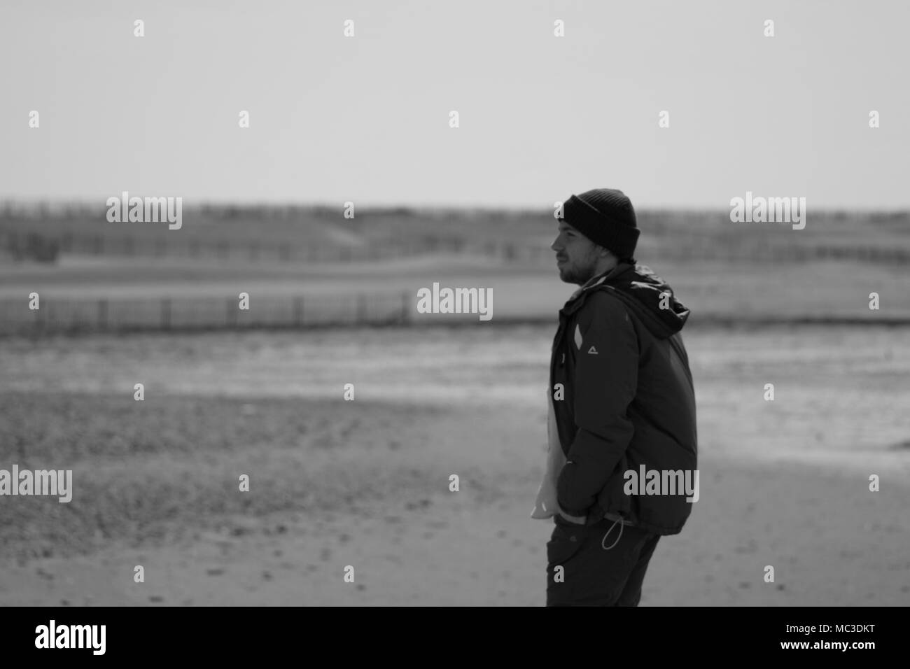 Jeune homme, marcher le long de la plage à Dawlish Warren, Devon, UK. Printemps, 2018. Noir et blanc. Banque D'Images