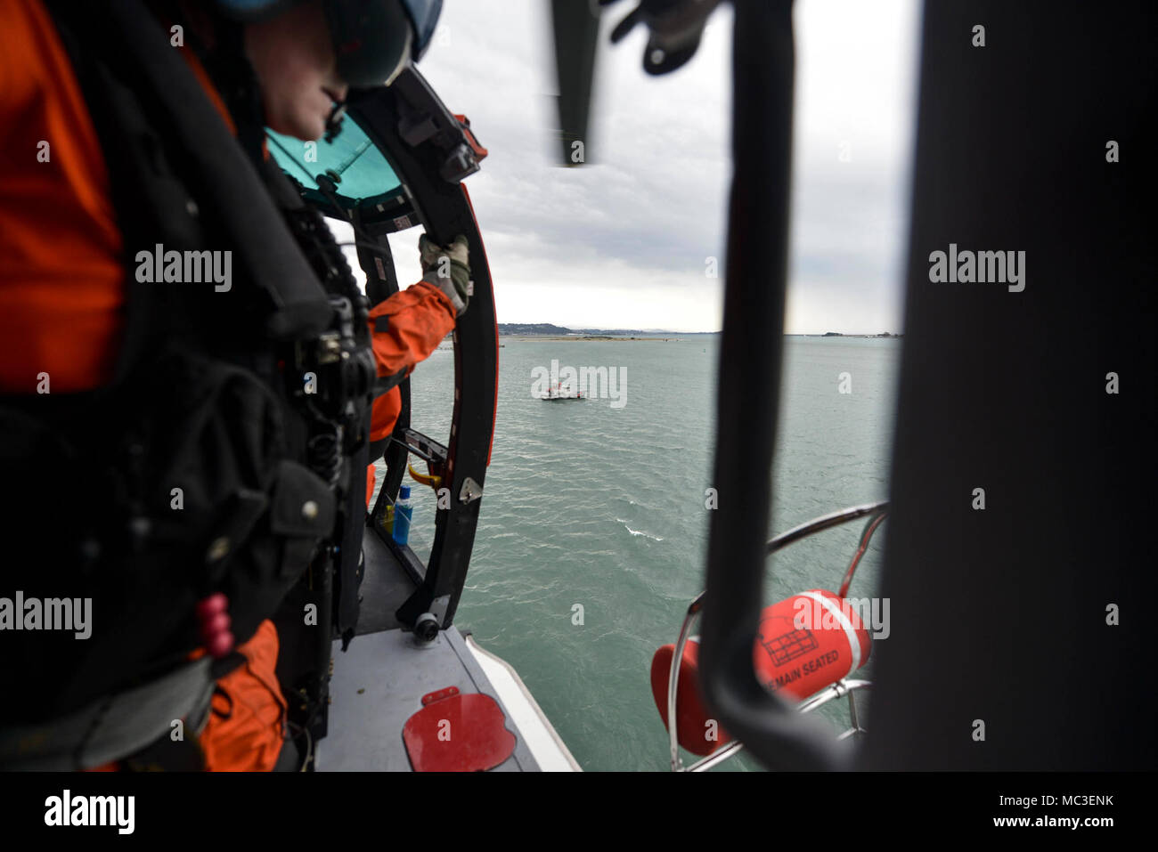 Un mécanicien de vol à bord d'un hélicoptère MH-65 de Dolphin Coast Guard Air Station Humboldt Bay à Eureka, Californie, se prépare à baisser une nacelle de sauvetage d'une embarcation à moteur de 47 pieds au cours de la formation de l'équipage, le 7 mars 2018. Les équipages des hélicoptères de la Garde côtière canadienne effectuent couramment des équipages de petits bateaux avec formation de maintenir leurs qualifications et ainsi que dans le cas d'une évacuation sanitaire demande d'un bateau ou navire, les équipages sont compétents dans leurs techniques de sauvetage. Banque D'Images