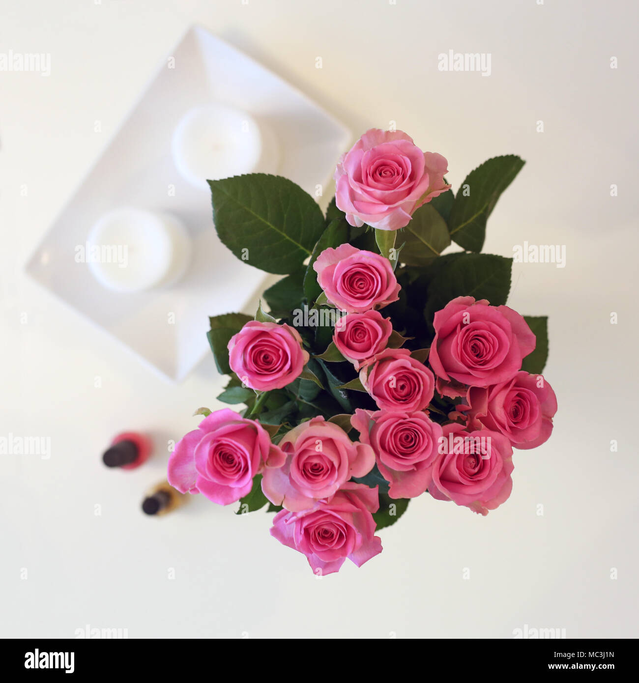 Un bouquet de fleurs roses dans un vase. La photo est prise d'en haut (flatlay). En plus il y a de roses bougies blanches et deux ongles. Banque D'Images