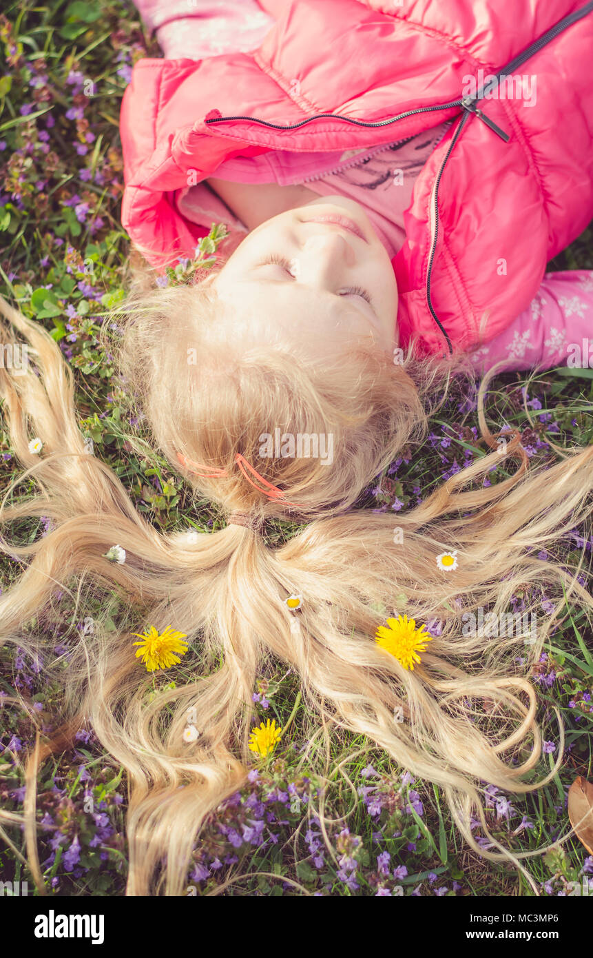 Adorable petite fille blonde avec de longs cheveux blonds couché dans la prairie de fleurs avec des fleurs dans les cheveux Banque D'Images