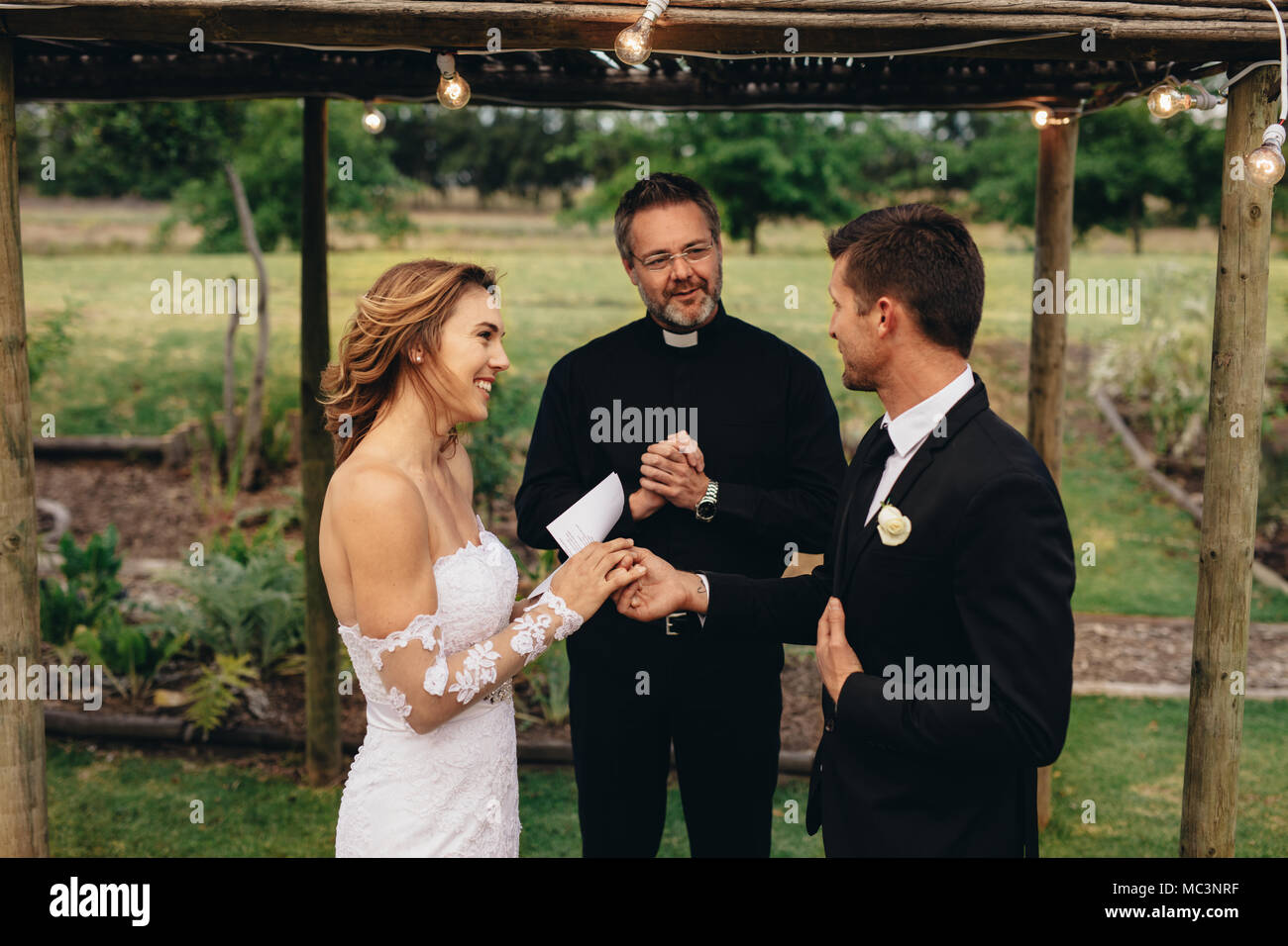 Heureux les jeunes mariés l'échange des vœux de mariage lors de la cérémonie du mariage en face de prêtre. La lecture de quelques vœux de mariage pour l'autre. Banque D'Images Heureux les jeunes mariés l'échange des vœux de mariage lors de la cérémonie du mariage en face de prêtre. La lecture de quelques vœux de mariage pour l'autre. Banque D'Images